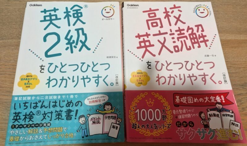 学研の参考書2冊が並んでいる写真。左側は水色と白のカバーの『英検2級をひとつひとつわかりやすく。』、右側はピンクと白のカバーの『高校英文読解をひとつひとつわかりやすく。』。木目のテーブルの上に置かれている。
